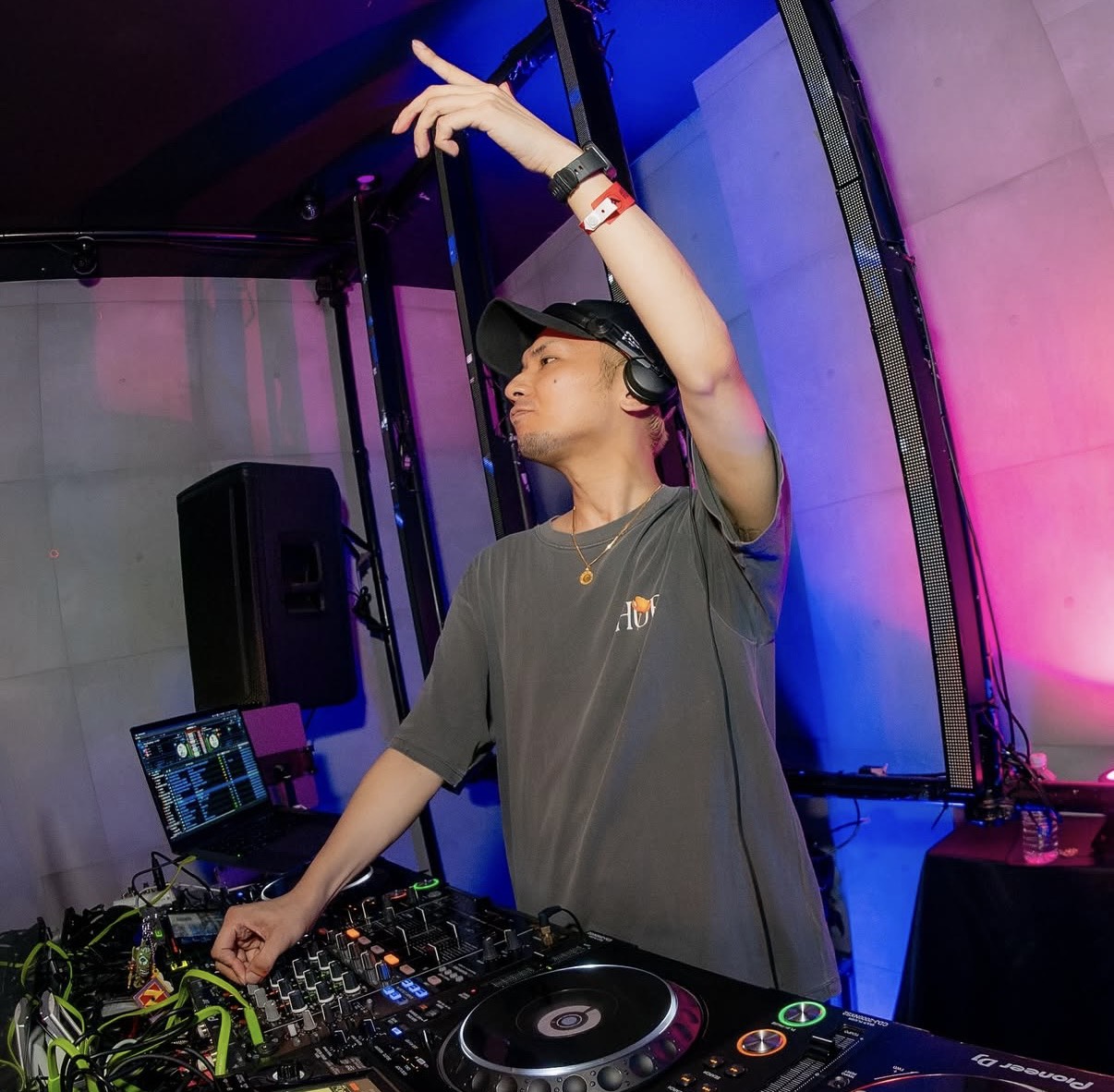 DJ機材の前で片腕を上げるHIDe