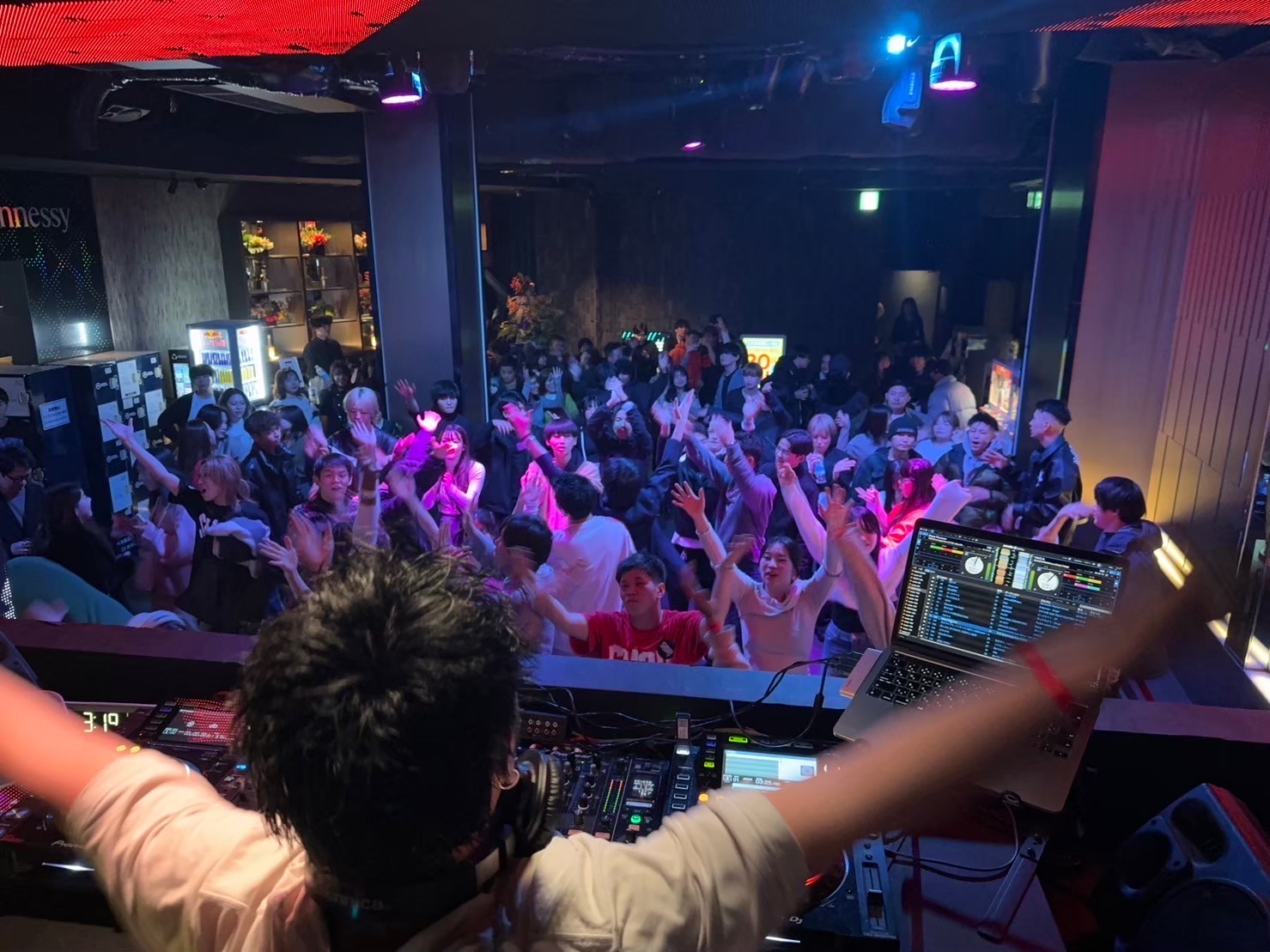 DJブースから客席へ両腕を広げるDJ 4⤴︎と、手を上げるお客さん