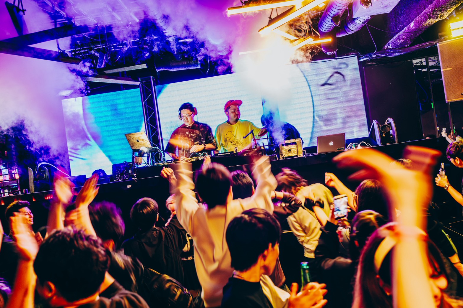 DJブースの前で、多くのお客さんが手を上げて盛り上がるフロア